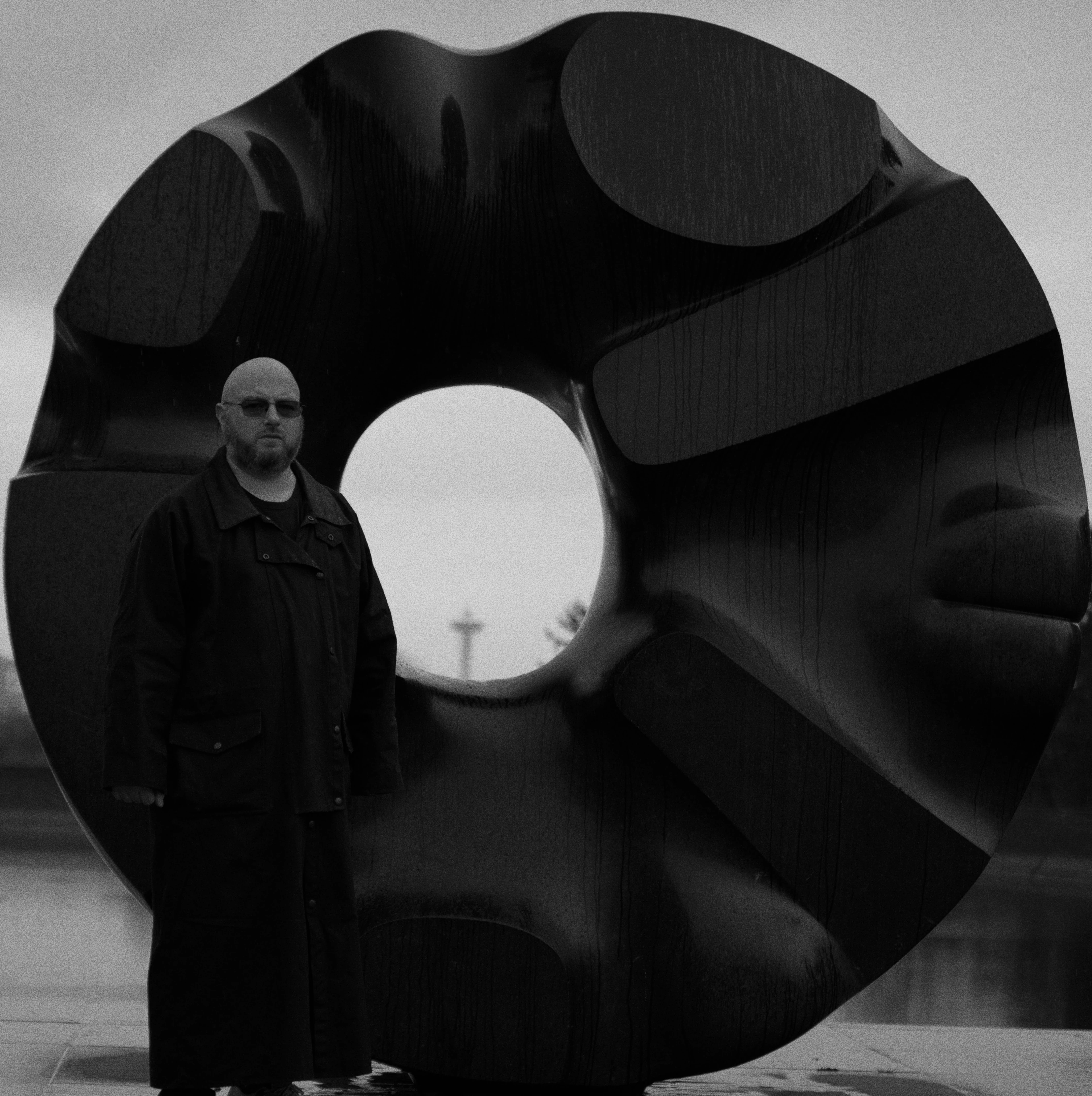 Portrait of Brad Herst, Principal Architect at Studio 206, standing before the Black Sun sculpture in Seattle.